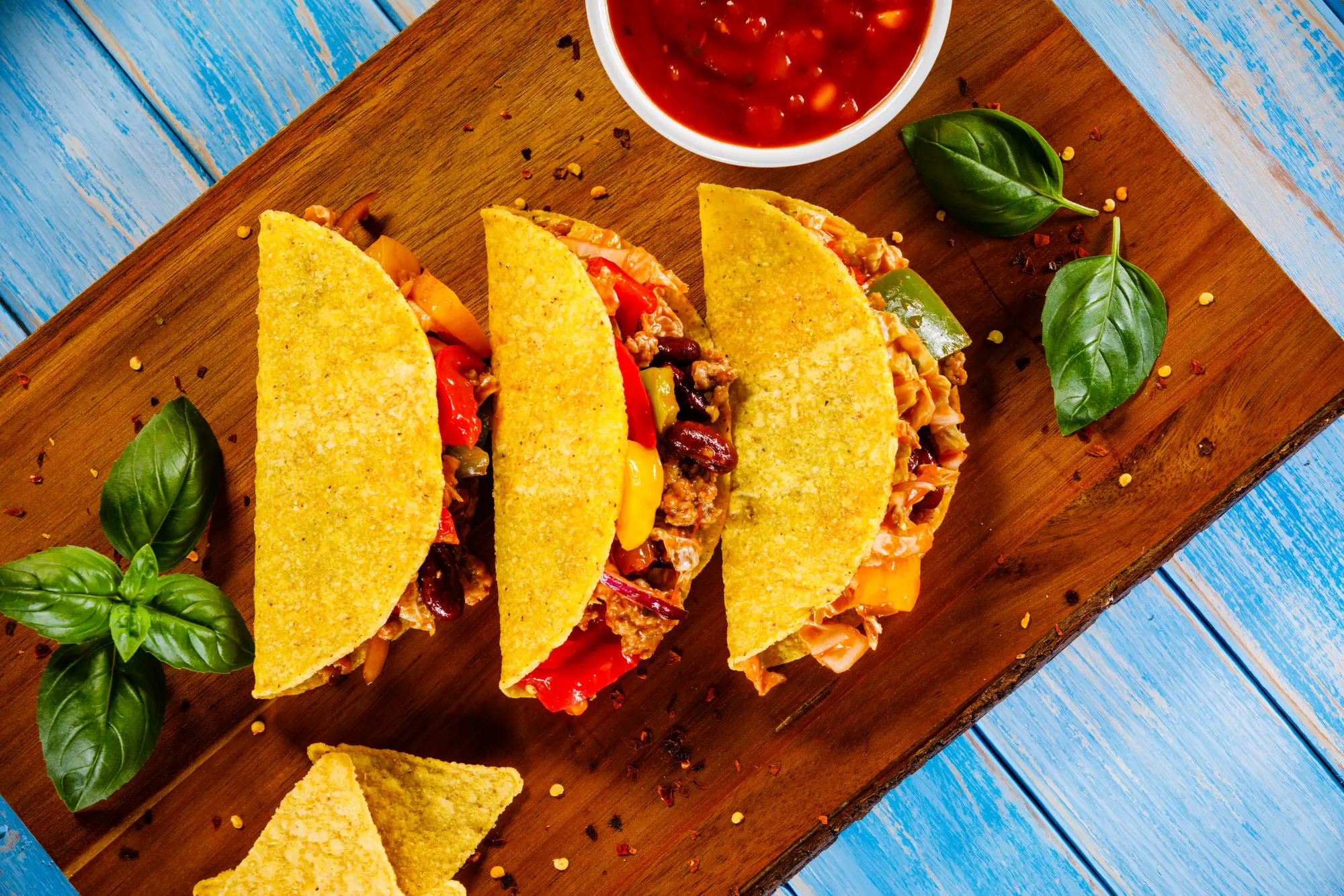 Drei gefüllte Tacos auf Holzbrett mit Salsa und Basilikum garniert