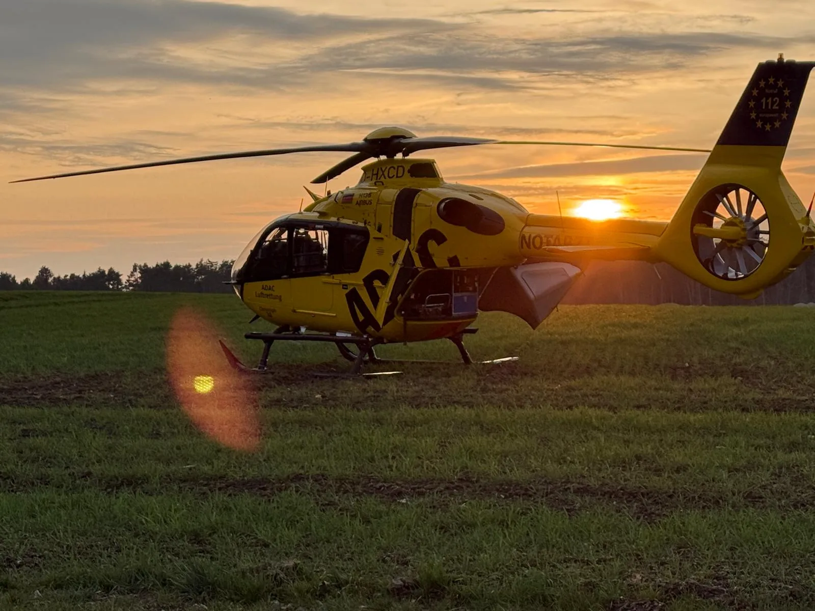 Rettungshubschrauber steht bei Sonnenuntergang auf einem Feld, gelb-schwarze Lackierung sichtbar.
