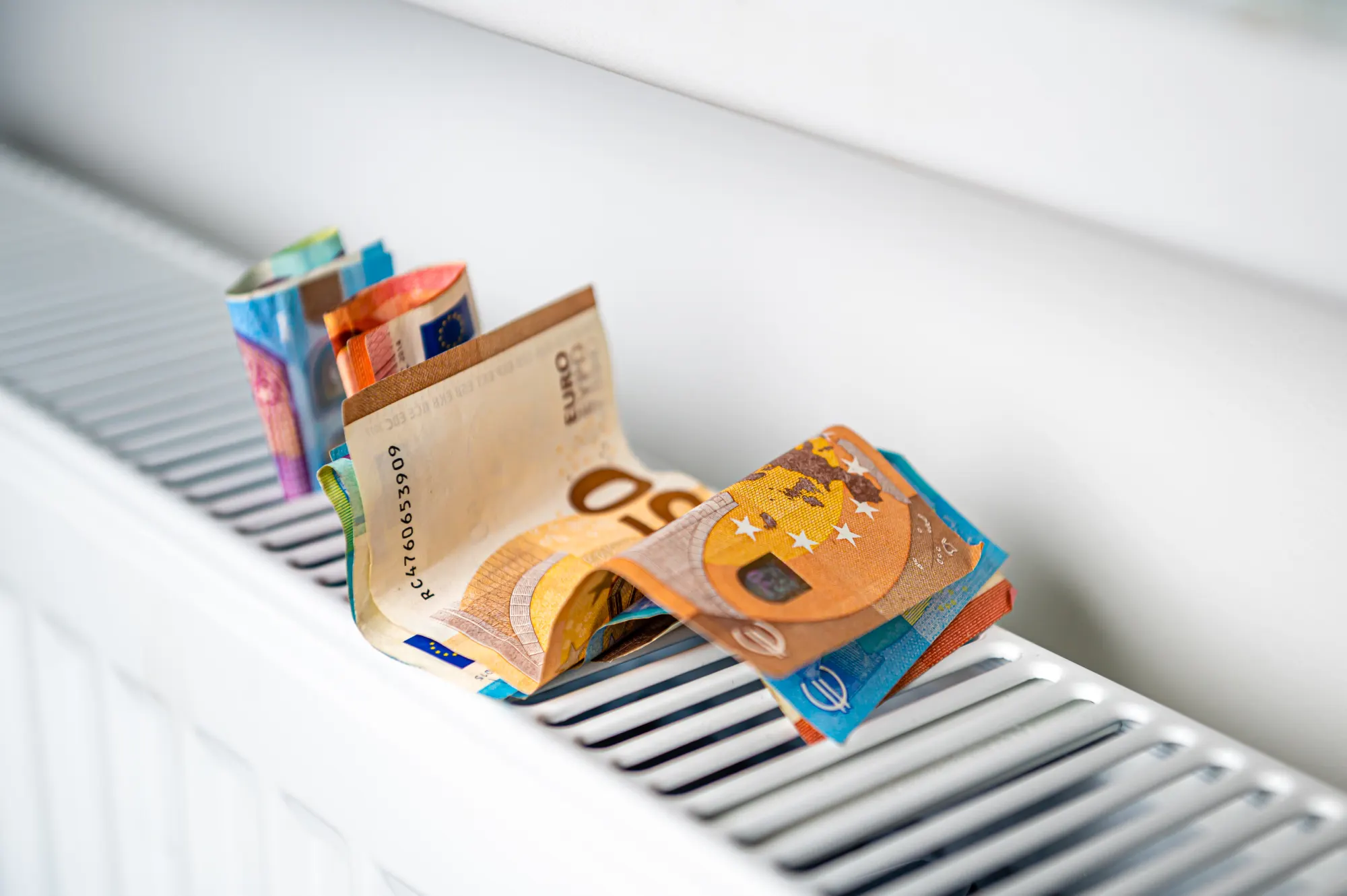 Mehrere Euro-Geldscheine liegen gefaltet auf einem weißen Heizkörper