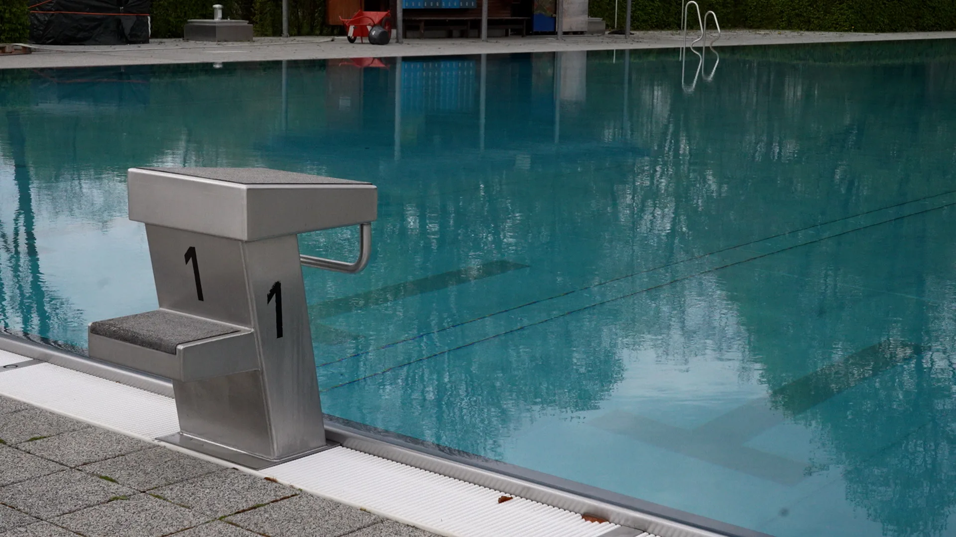 Startblock mit der Nummer 1 an einem Schwimmbecken mit türkisblauem Wasser und Schwimmbahnmarkierungen.