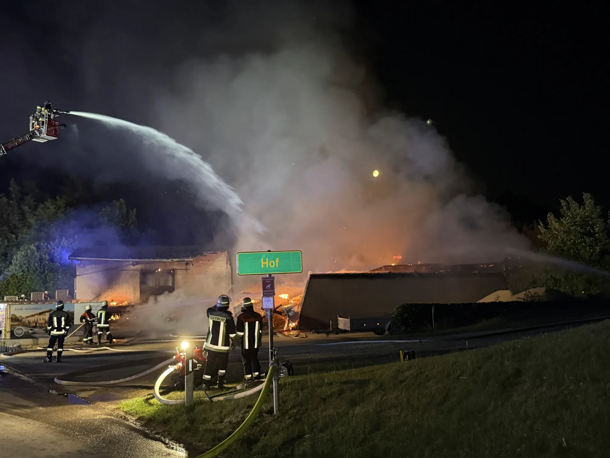 Feuerwehrleute bekämpfen Großbrand in landwirtschaftlichem Betrieb mit Drehleiter und Wasserschläuchen