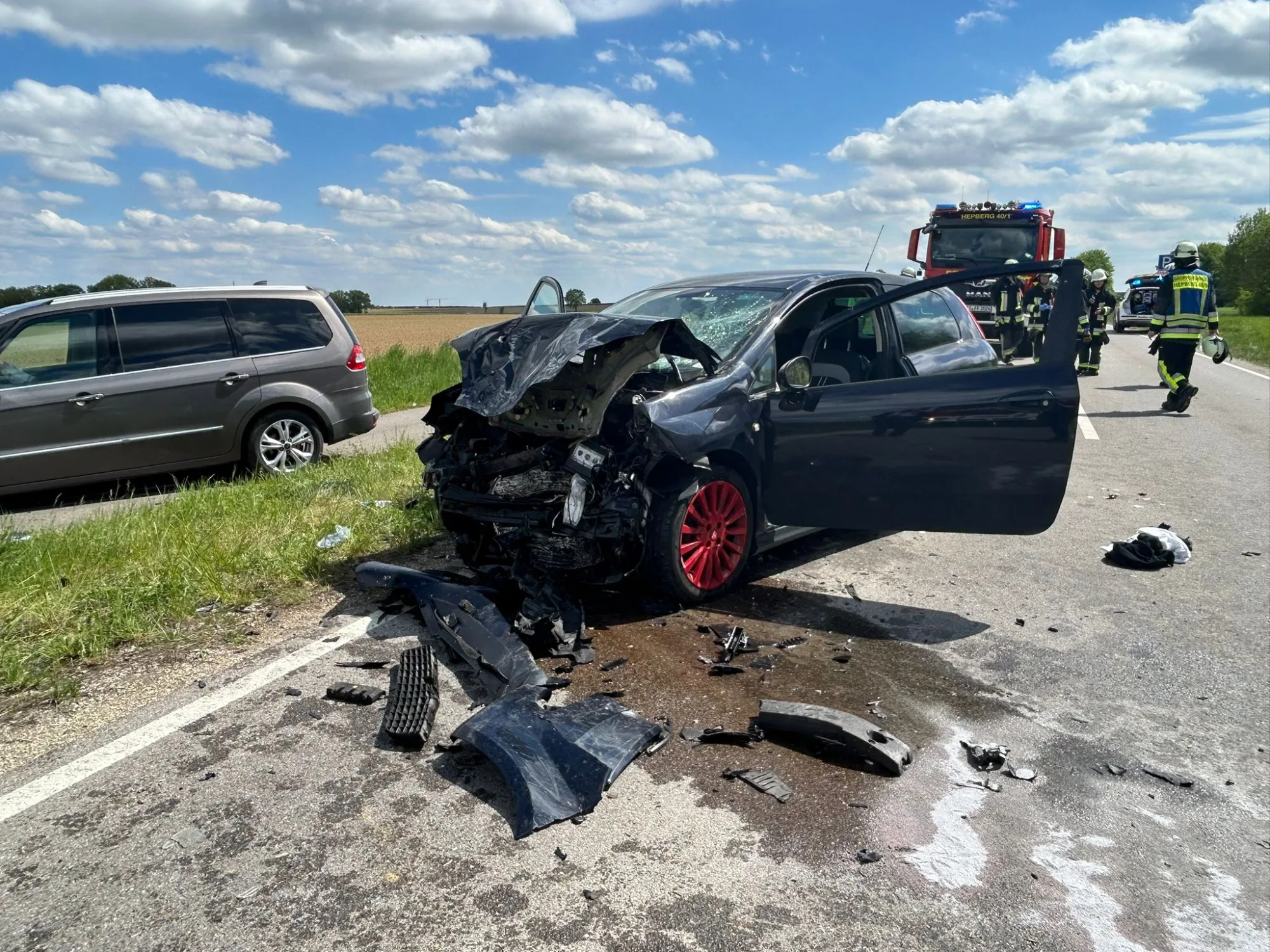Schwerer Verkehrsunfall mit stark beschädigtem Auto und Trümmerteilen auf der Straße, Rettungskräfte im Einsatz