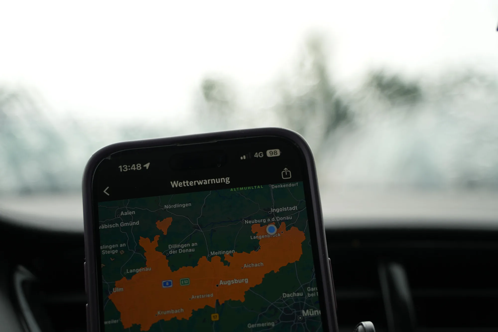 Smartphone zeigt Wetterwarnung-App mit farbkodierter Karte, orangefarbene und grüne Bereiche sichtbar