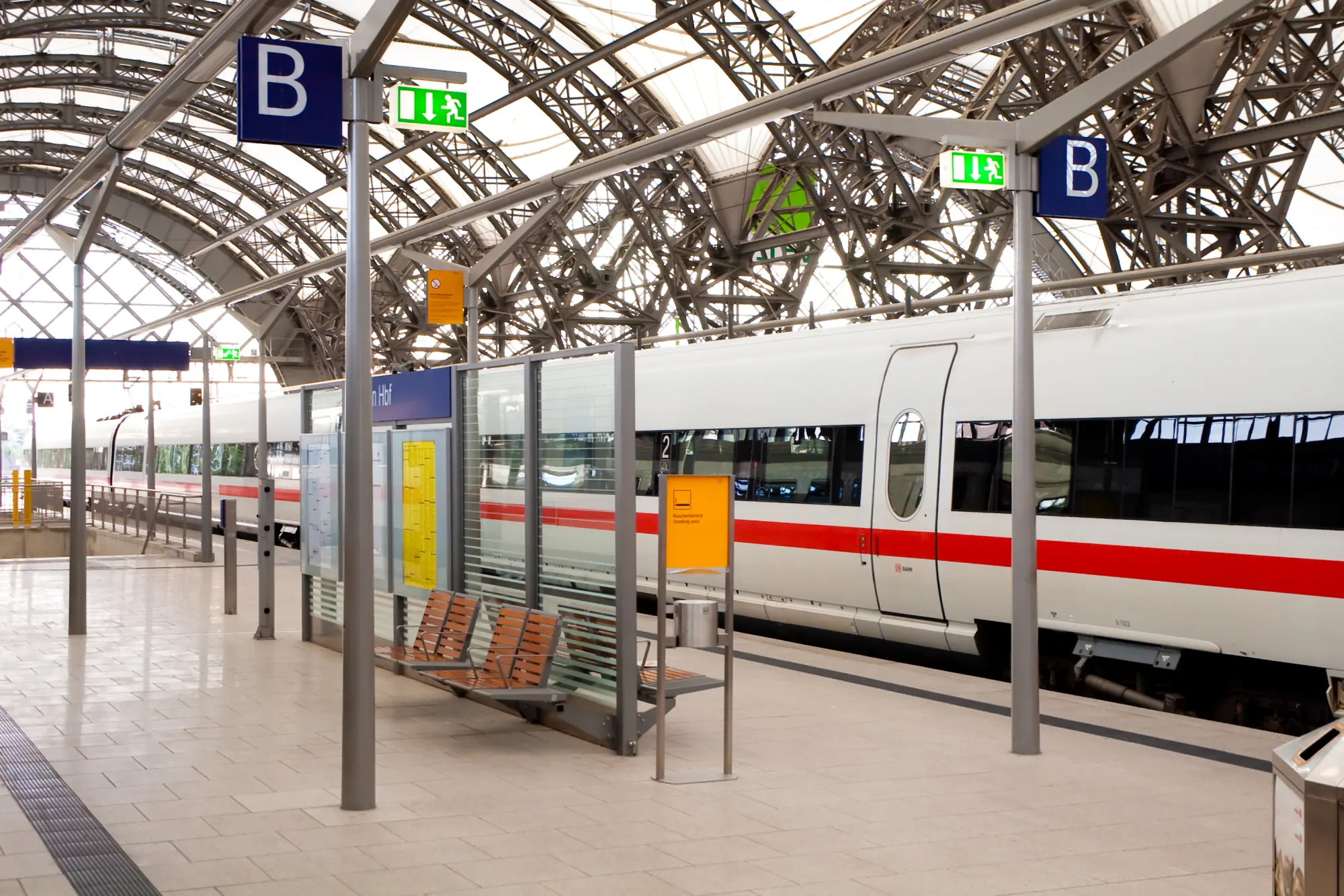 Moderner Fernzug steht am Bahnsteig unter einer Glasdachkonstruktion, Wartebänke und Bahnsteigschilder sichtbar