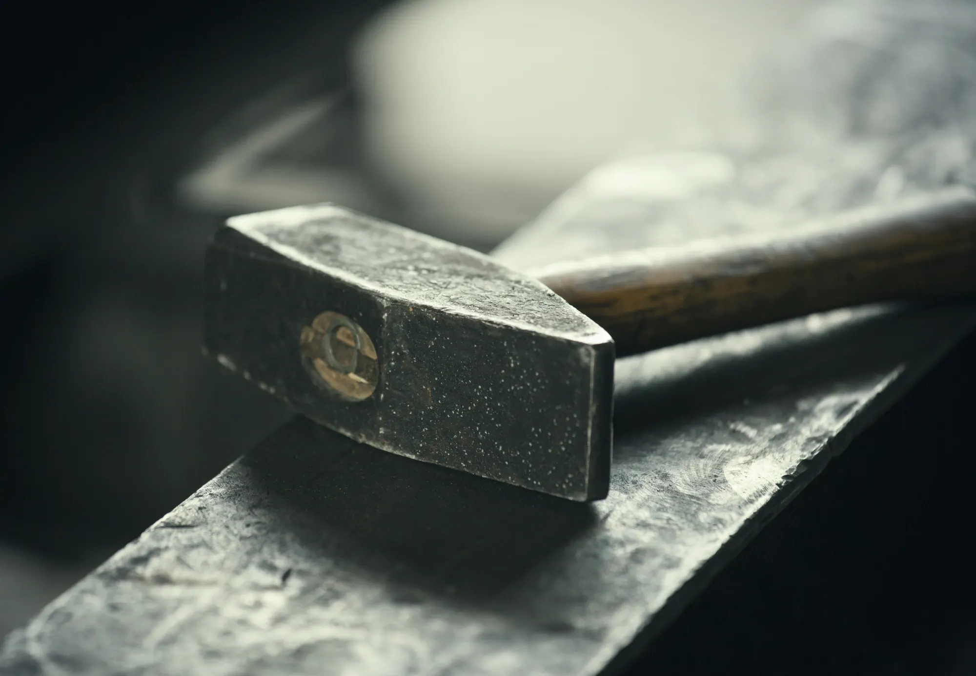 Schwarzer Hammer mit Holzstiel liegt auf einer Werkbank in einer Werkstatt
