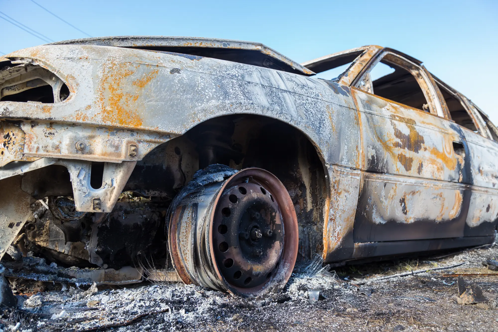 Ausgebranntes Autowrack auf asphaltierter Straße, Karosserie stark beschädigt und verrostet