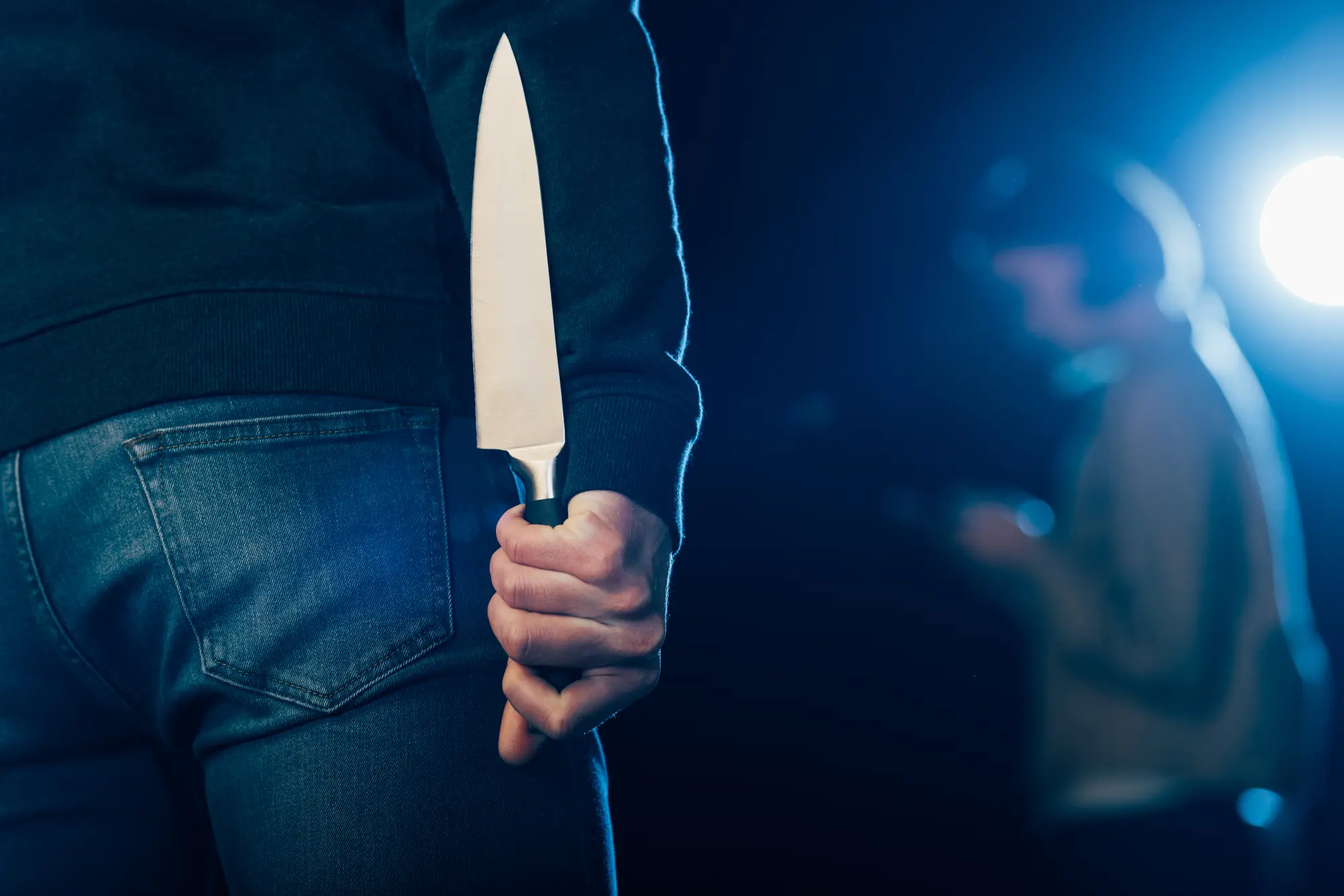 Person hält Messer hinter dem Rücken bei nächtlicher Straßenbeleuchtung