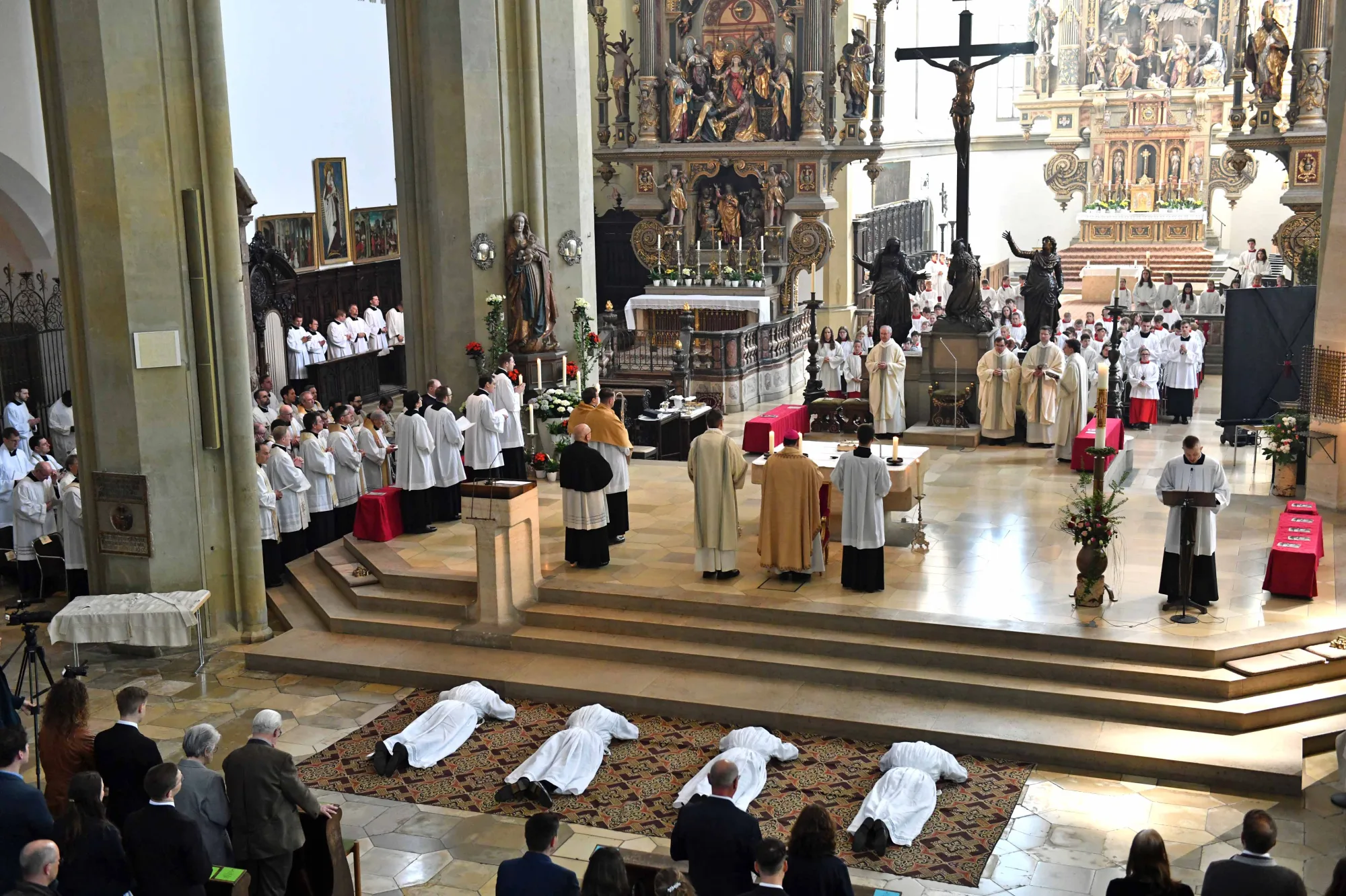 Priesterweihe in einer Kathedrale mit mehreren Kandidaten, die vor dem Altar knien, umgeben von Geistlichen