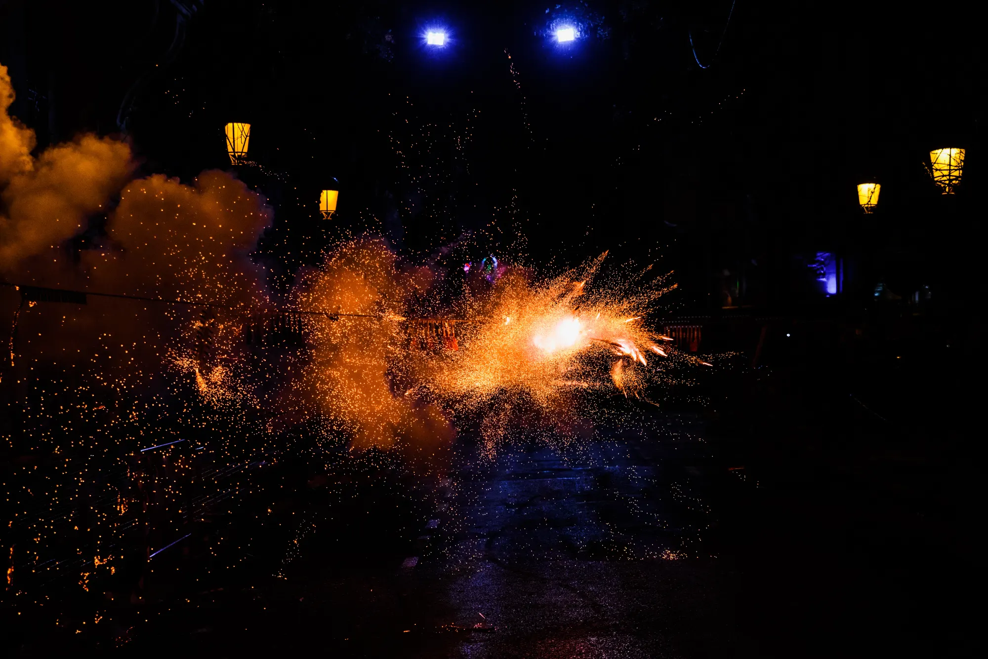 Feuerwerk mit orangen Funken vor dunklem Nachthimmel, im Hintergrund sind Straßenlaternen zu sehen