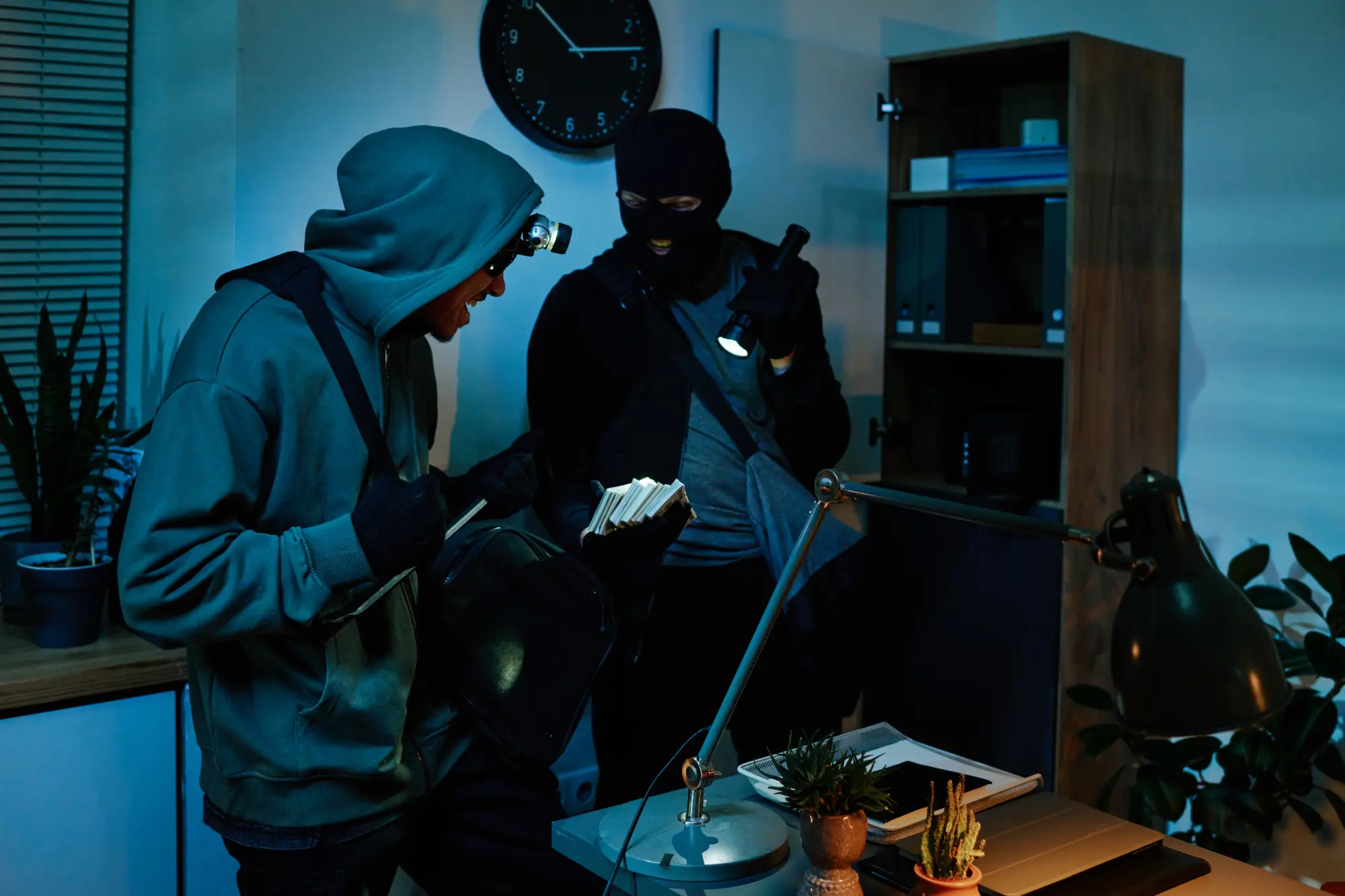 Zwei maskierte Personen durchsuchen nachts ein Büro mit Taschenlampen und nehmen Dokumente mit