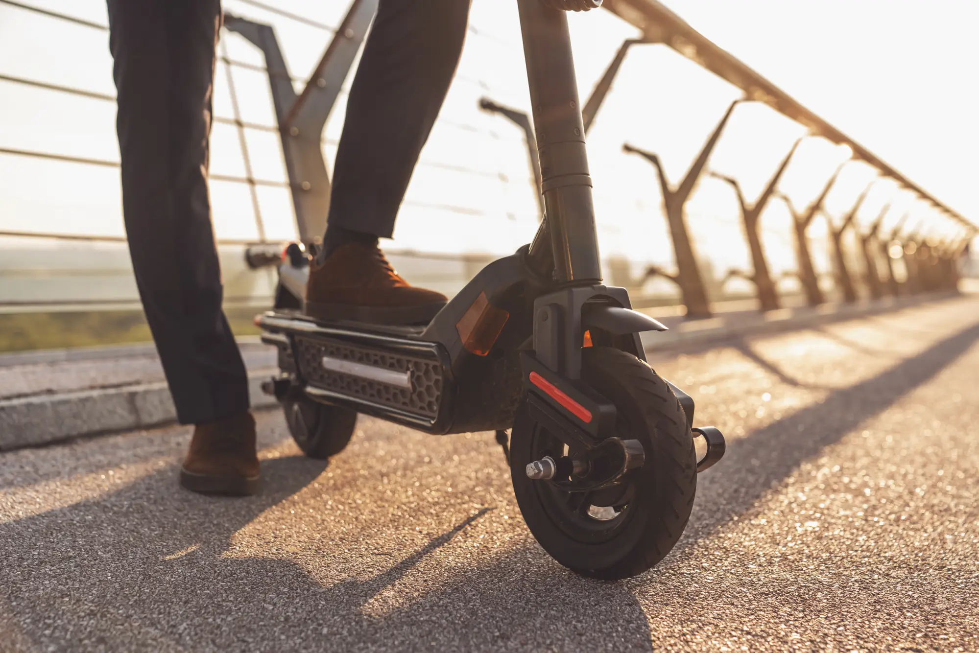 Person steht neben E-Scooter auf Brücke, Blick auf Beine und Elektroroller
