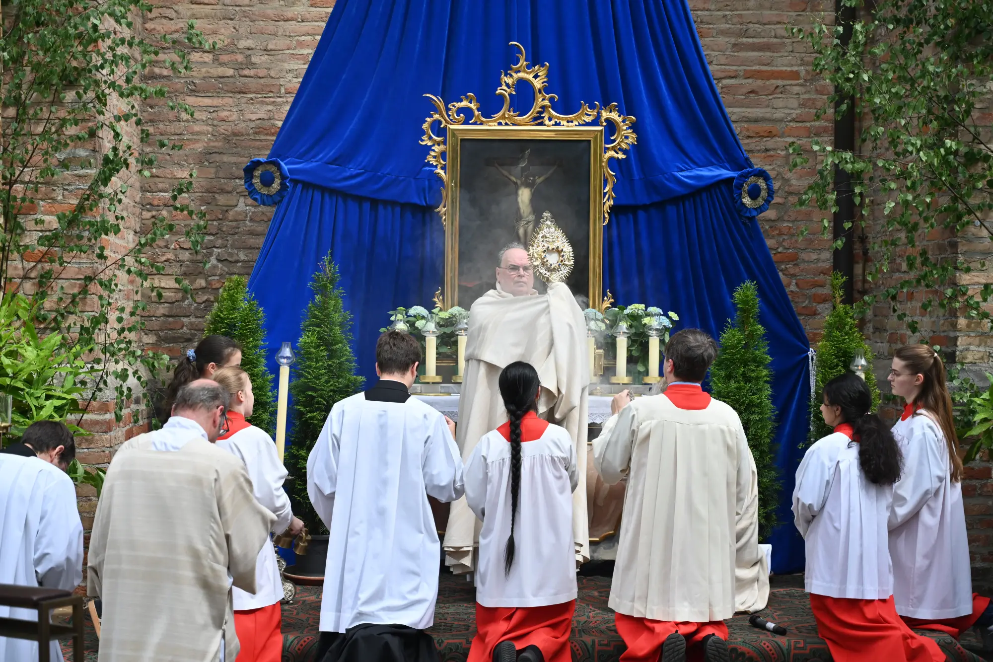 Bischof Dr. Bertram Meier hält Monstranz hoch vor Altar mit blauem Baldachin, Ministranten knien in weißen Gewändern davor