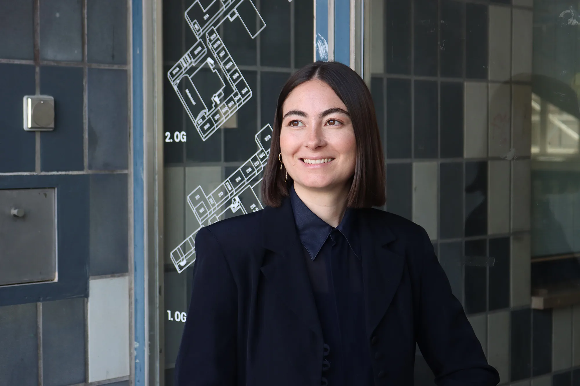Melina Hüttner lächelt vor Glaswand mit Gebäudegrundriss-Grafik