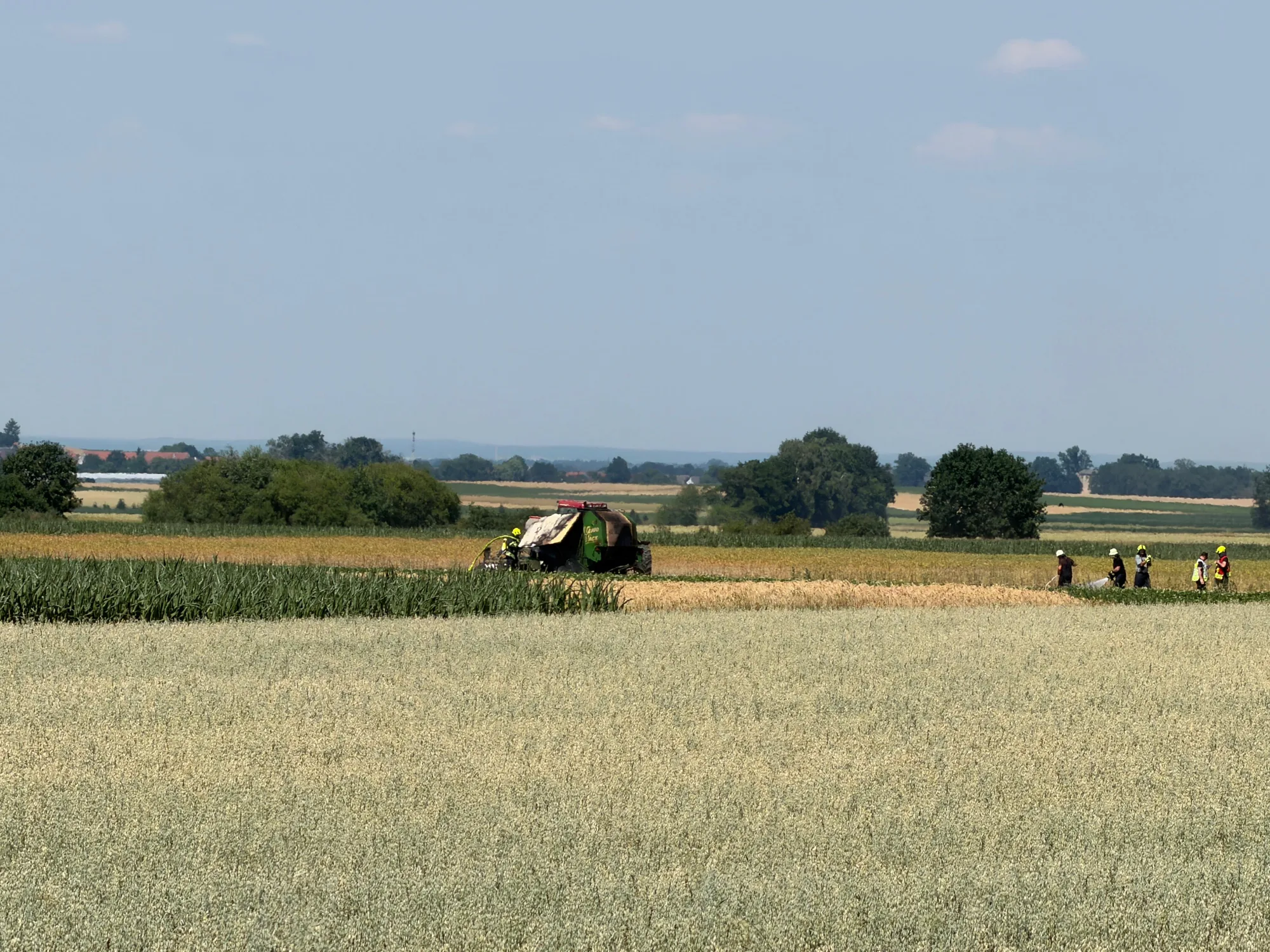 Strohballenpresse steht auf einem Feld, daneben stehen Feuerwehrleute